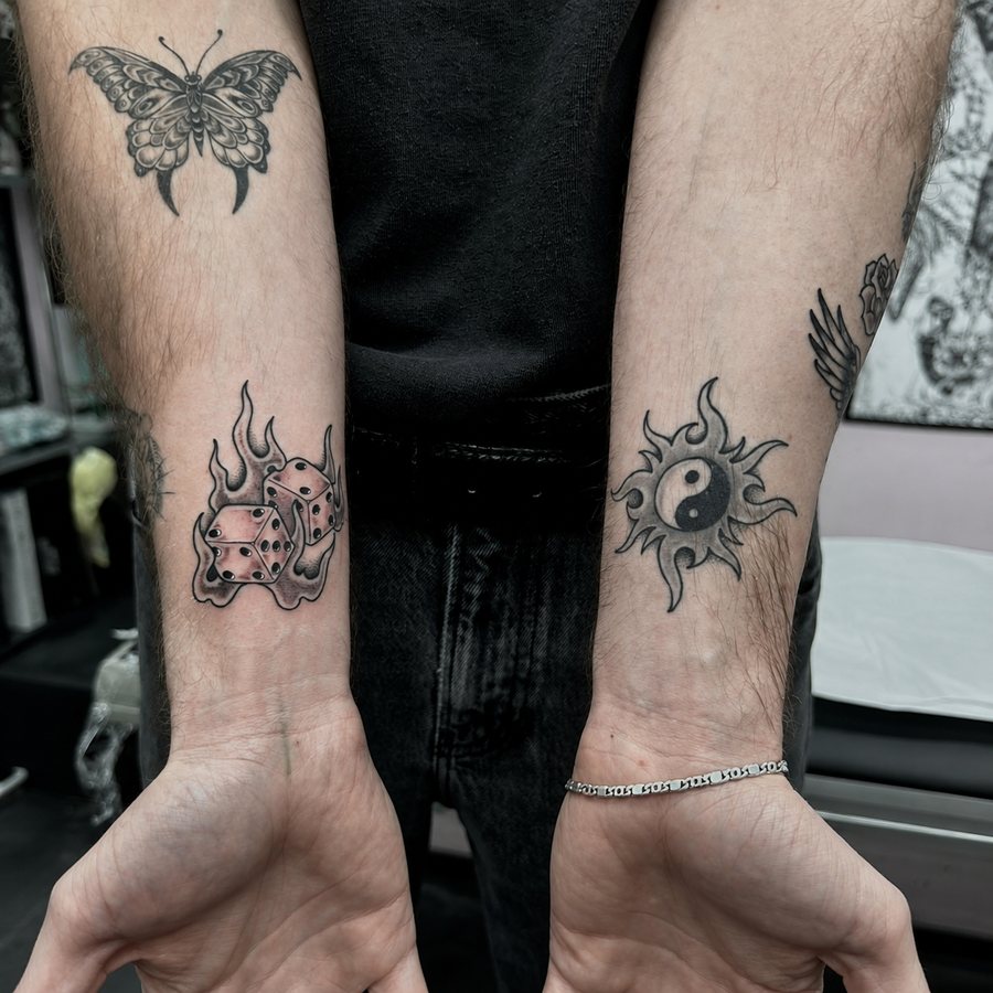 Several tattoos on both forearms, including a butterfly, dice and sun