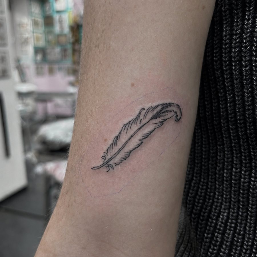 Fine-line feather tattoo on an arm