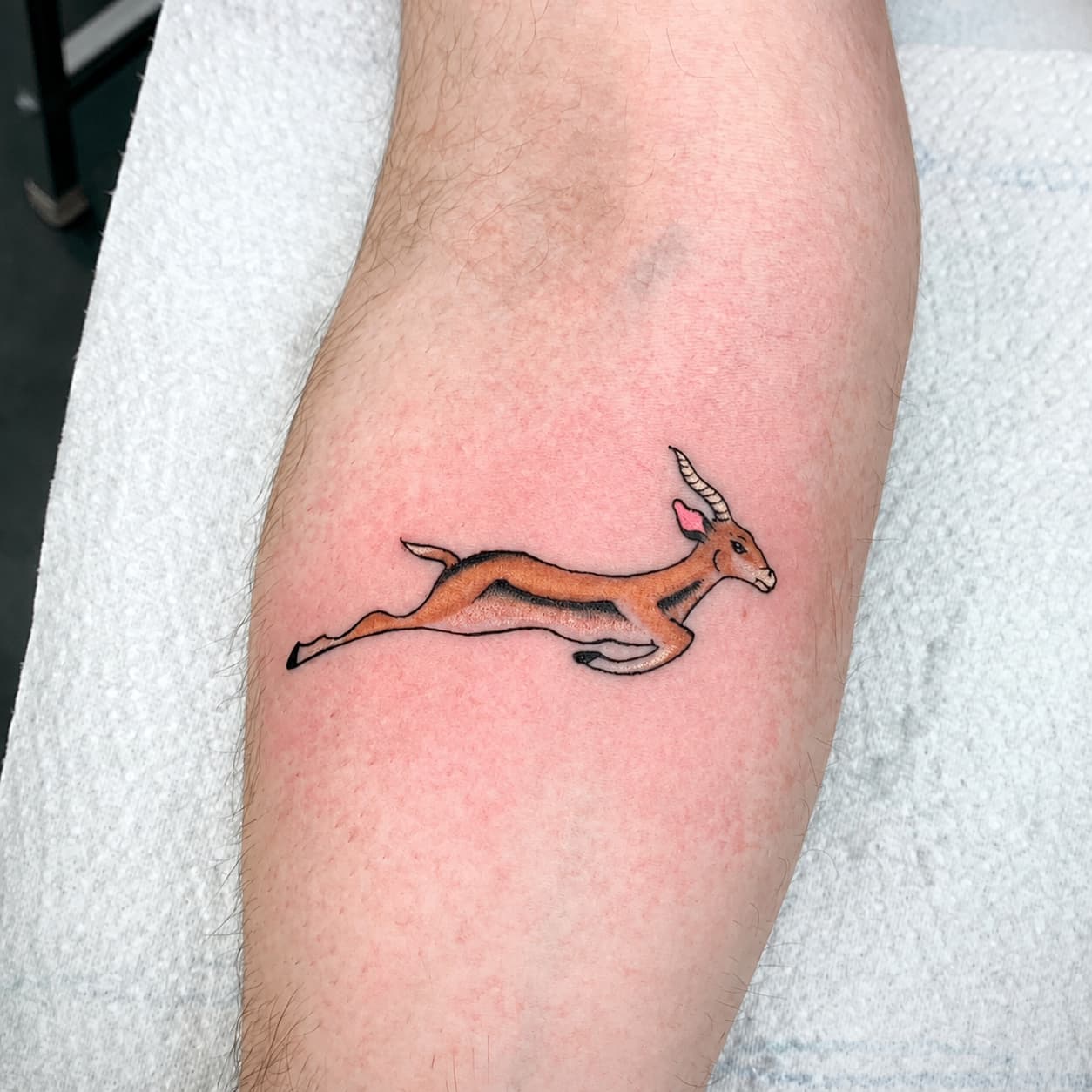 Colorful leaping horned animal tattoo with an orange body