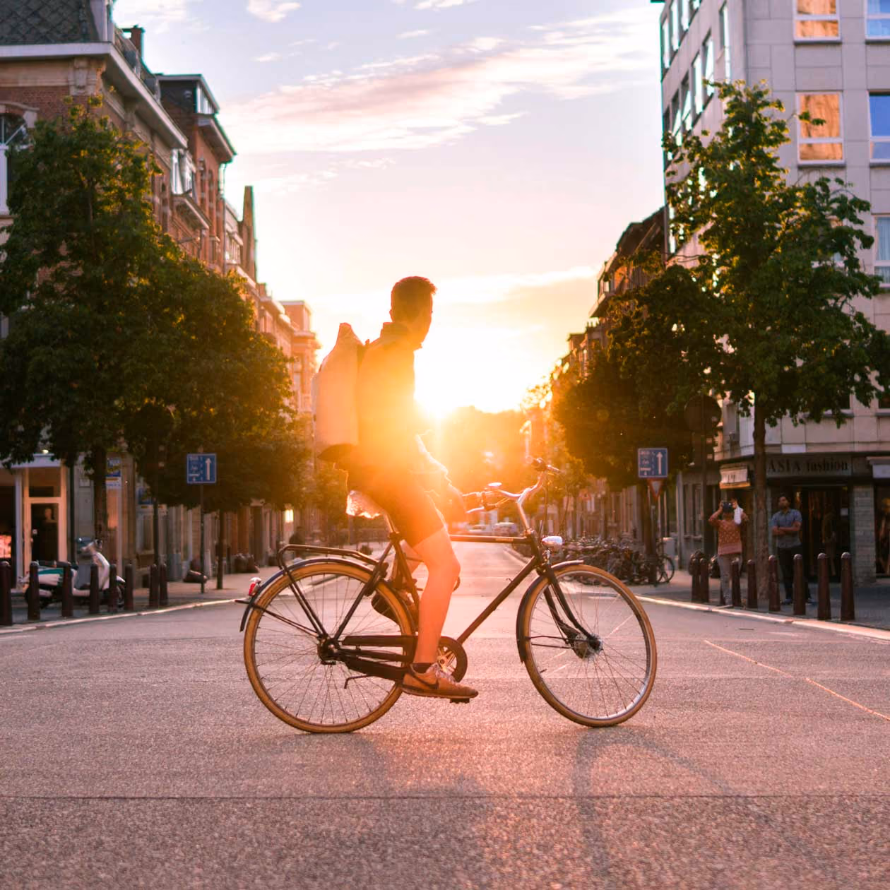 Person cyklar i stadsgata vid solnedgång med ryggsäck och kortbyxor.