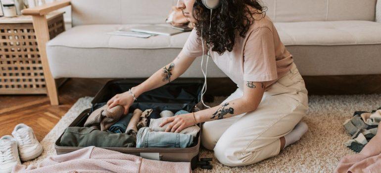 a woman listening to music as she packs her clothes inside a suitcase
