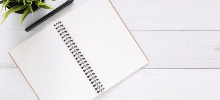 an opened notebook standing on the wooden table with a plant nearby
