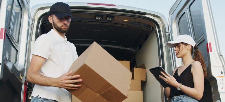 two people loading a moving van with cardboard boxes