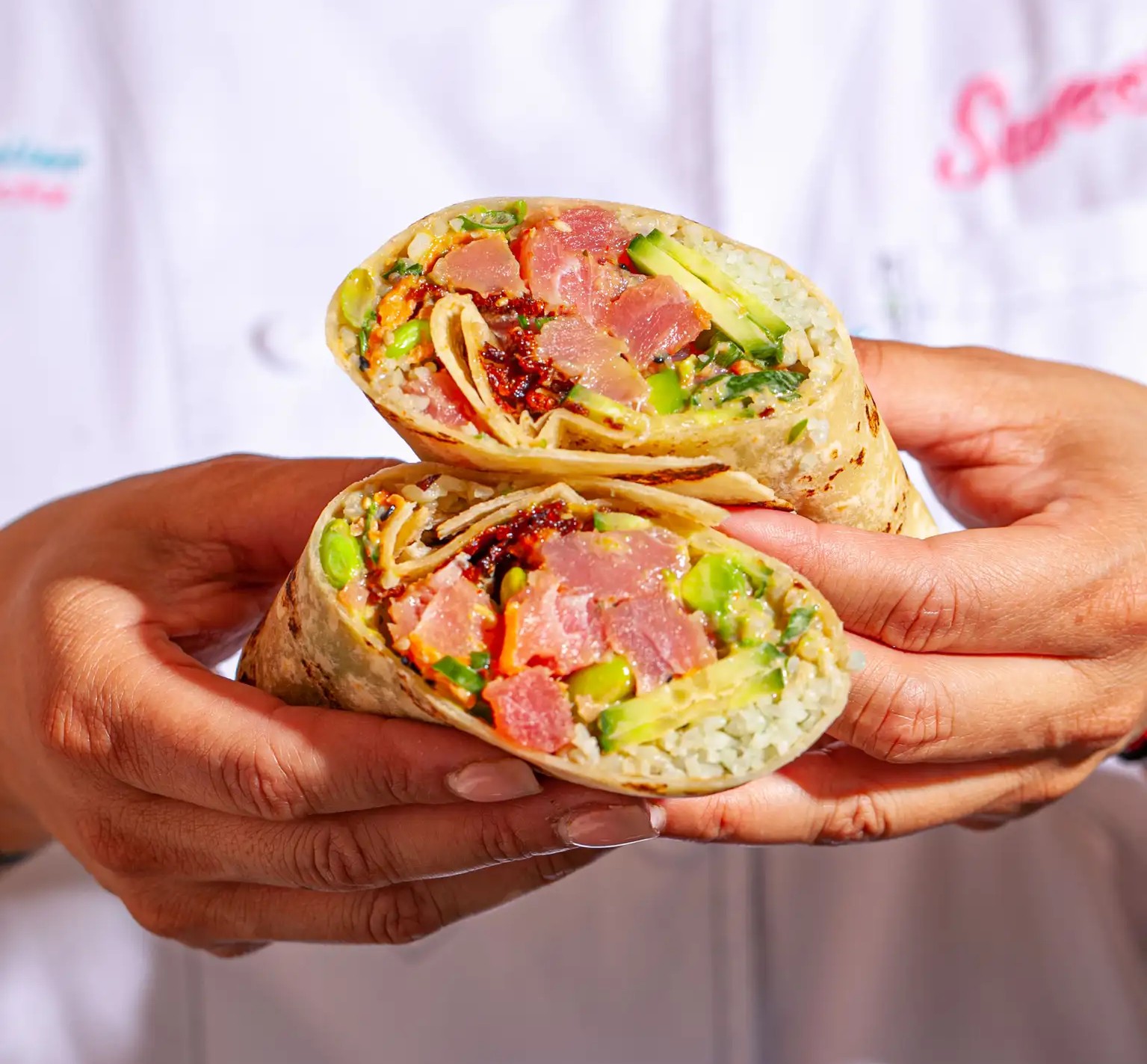 Close-up of hands holding a half-cut burrito prepared at Sweetfin. 