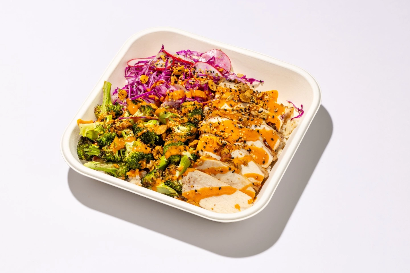 Spicy Chicken Bowl with roasted broccoli, sesame-ginger slaw, and garnish in white takeout container