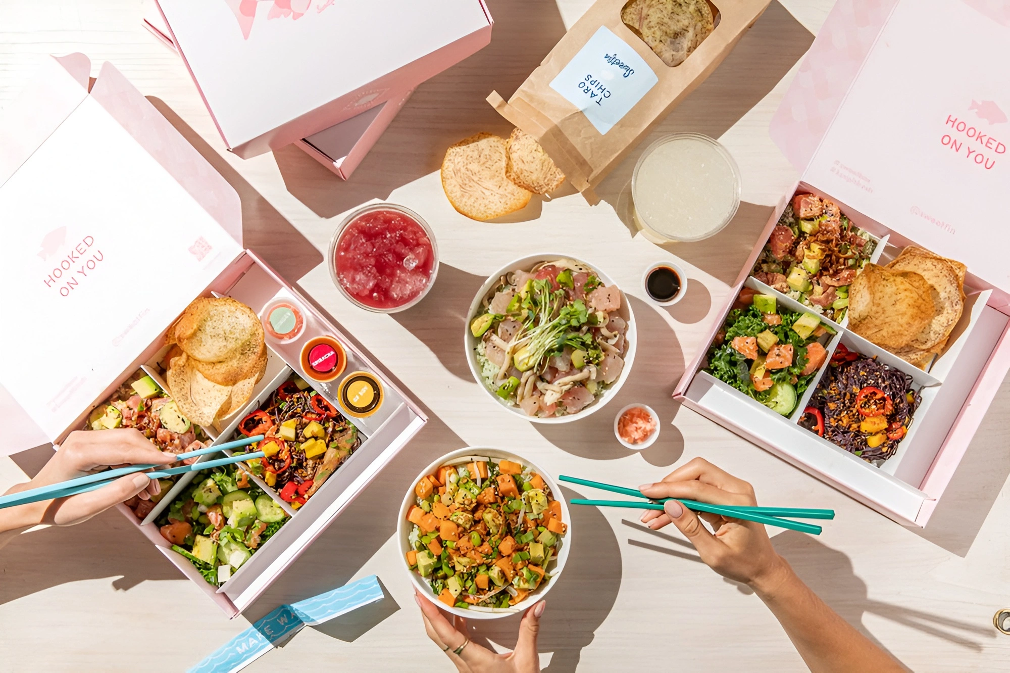 Sweetfin poke bowls and catering spread with fresh fish, avocado, vegetables, chips, drinks, and chopsticks.