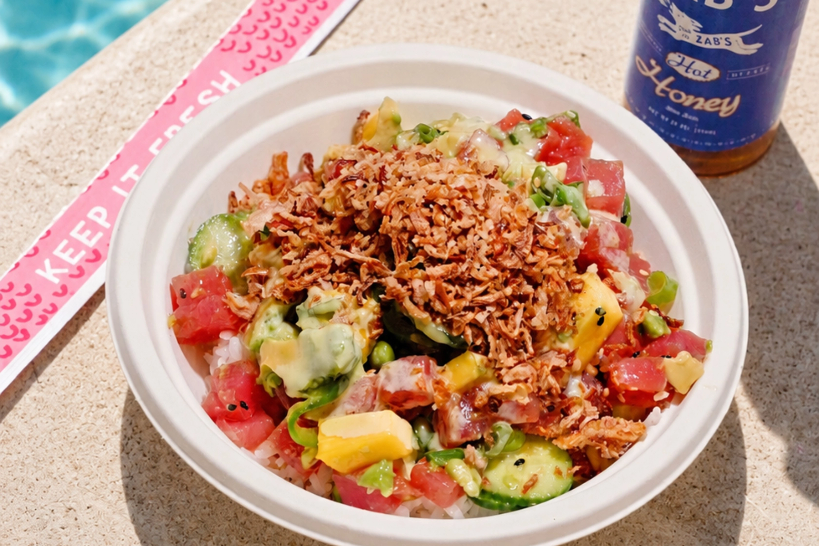 Sweetfin poke bowl with fresh tuna, mango, cucumber, avocado, crispy shallots, and rice served poolside with hot honey.