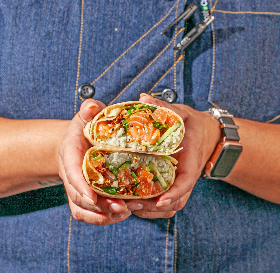 Sweetfin salmon poke burrito cut in half with sushi rice, cucumber, and fresh salmon, held for a handheld lunch.