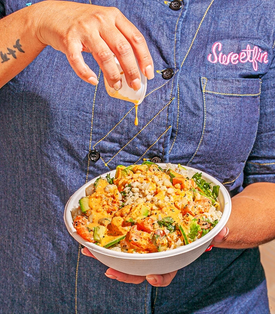  Sweetfin poke bowl with avocado and sauce, held by a team member in a Sweetfin uniform