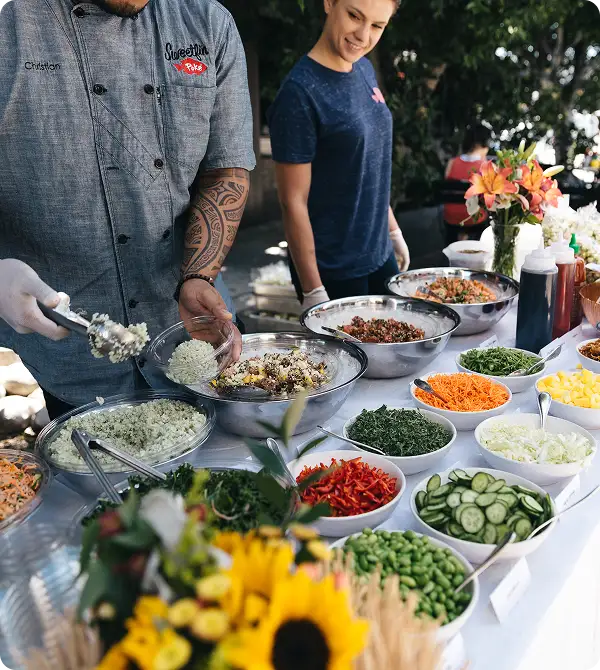 Sweetfin team preparing customizable poke bowls with fresh vegetables, rice, and toppings at an outdoor serving table.