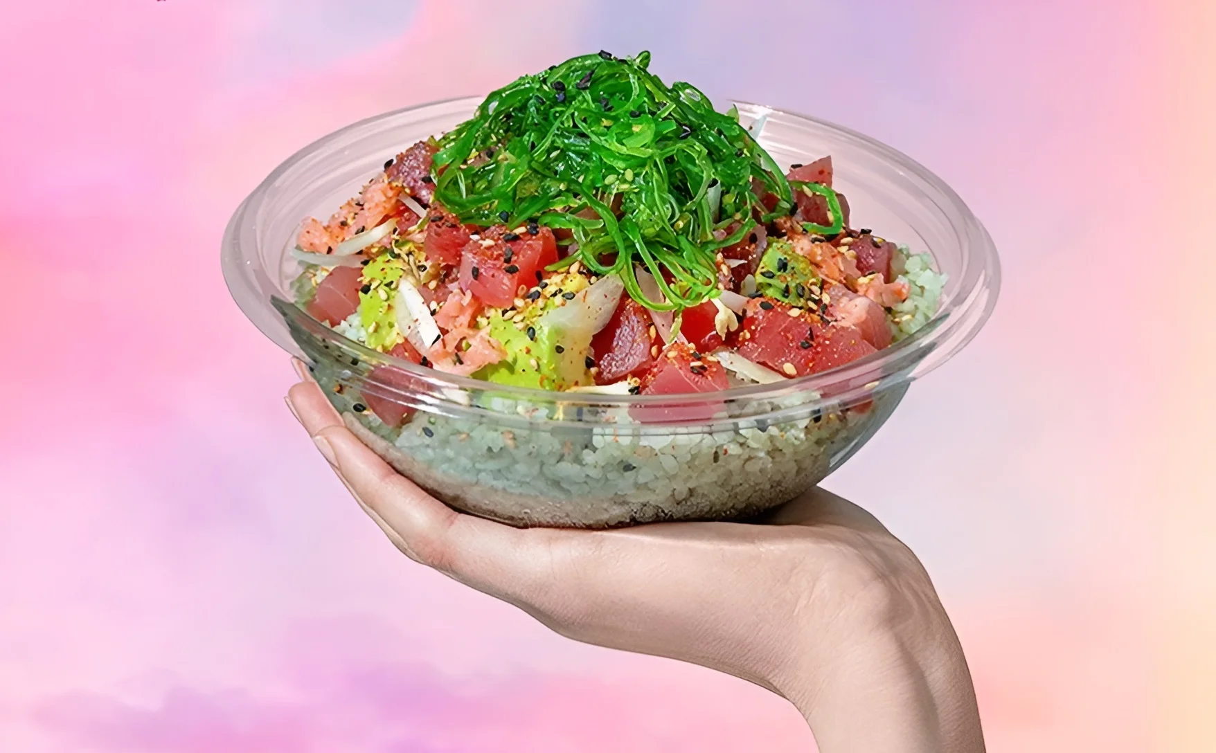 Sweetfin poke bowl with tuna, avocado, seaweed salad, and green bamboo rice held against a pink background.