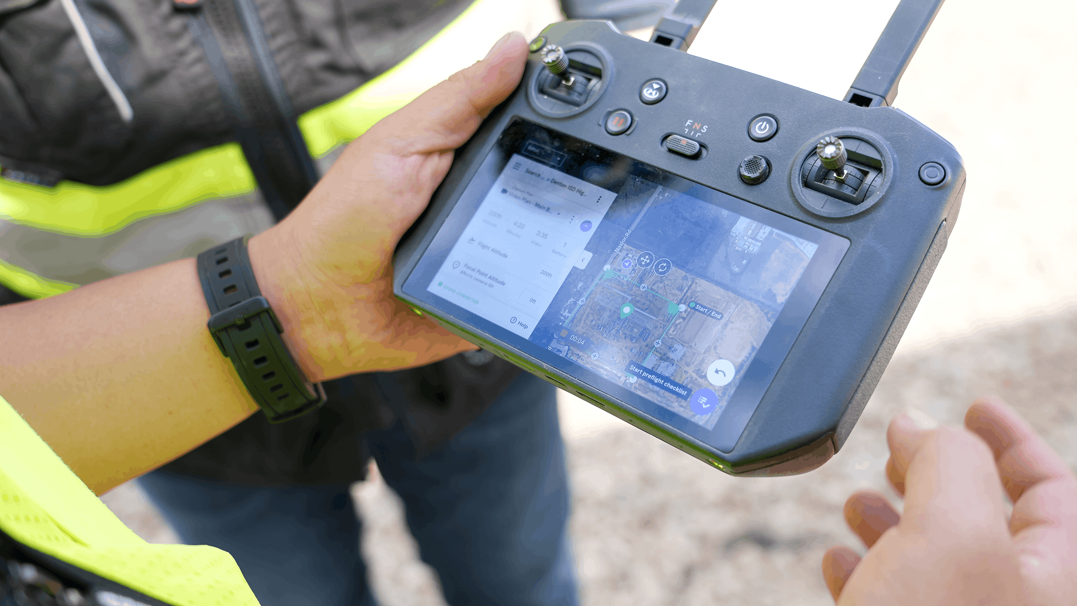 The image shows a person's hands holding a drone remote controller. The controller has a large displ...