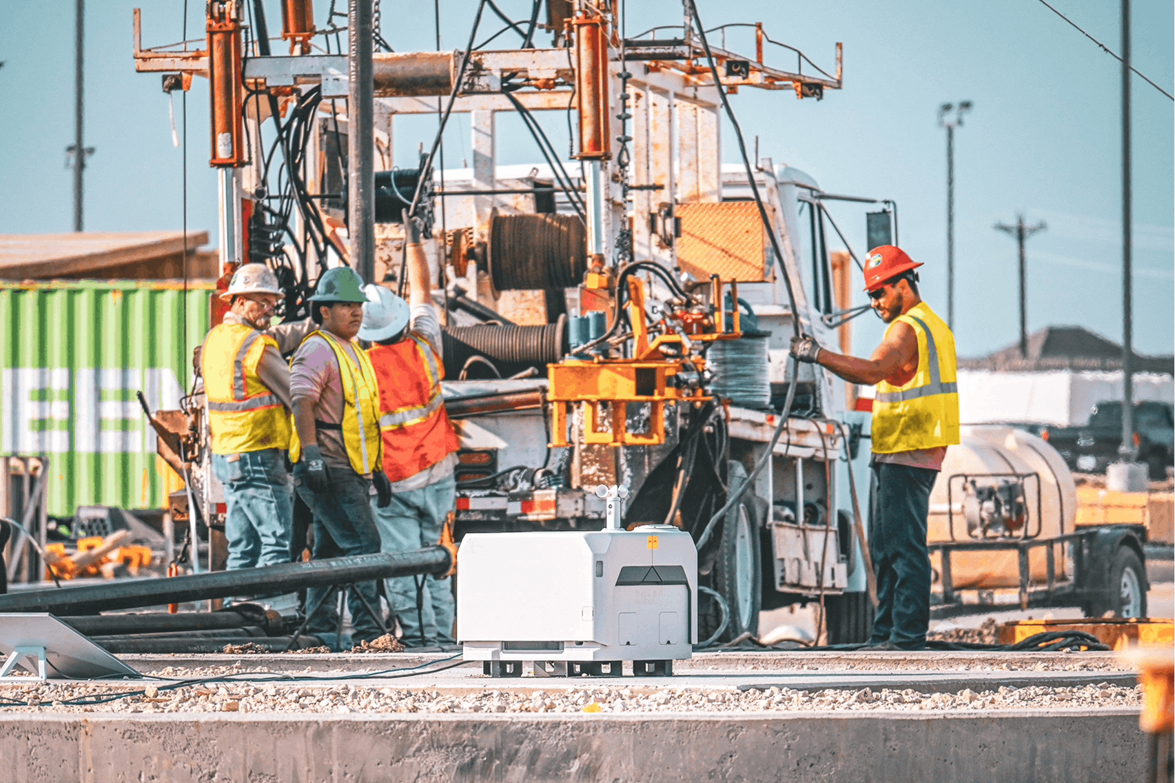 The image depicts a construction site with several workers wearing safety gear, including hard hats ...