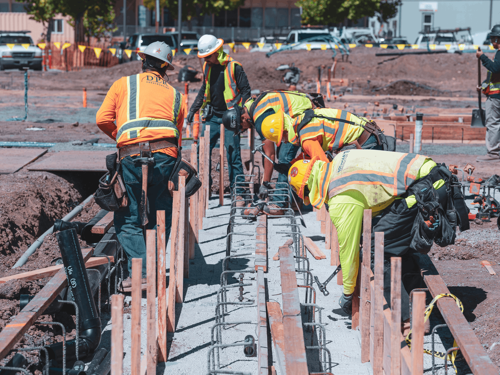 The image depicts a construction site with several workers wearing high-visibility safety gear, incl...