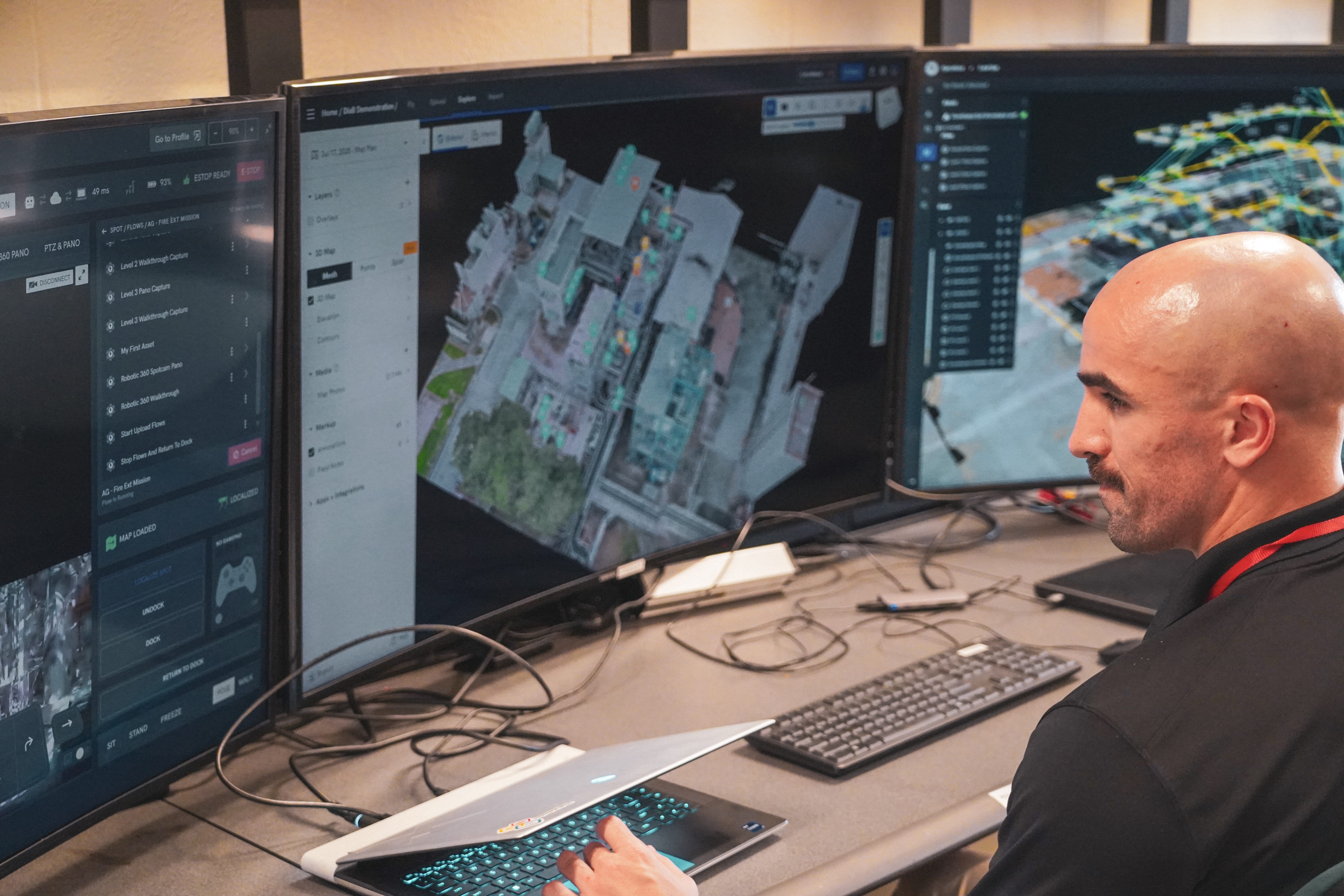 A professional workspace displays a man with a beard wearing a black shirt with red accents, seated ...