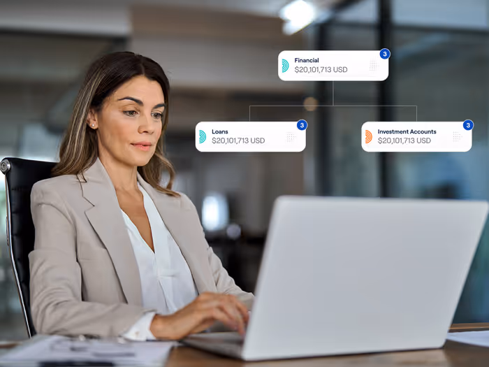 Businesswoman sitting at desk, working on laptop with financial chart overlays showing $20,101,713 USD in financial, loans, and investment accounts.