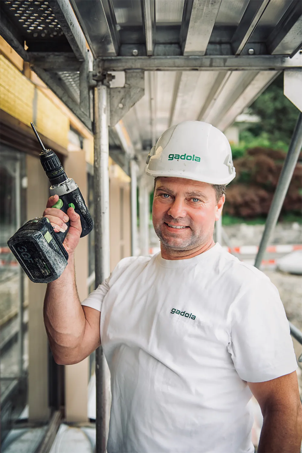 Gadola Bauarbeiter mit Bohrmaschine auf einem Gerüst