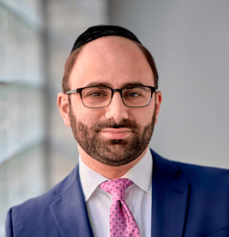 Brett Siegal picture. He's wearing suit and tie and a dark kippah, staring at the camera.