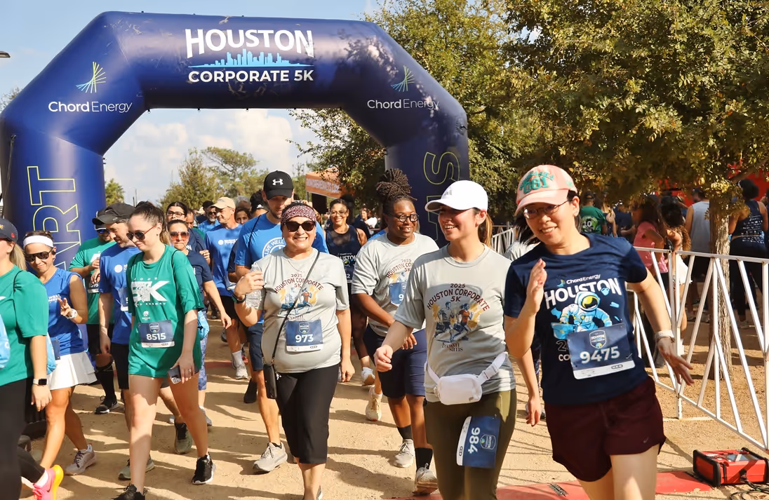 Diverse group of runners starting the Houston Corporate 5K race under a blue inflatable arch.