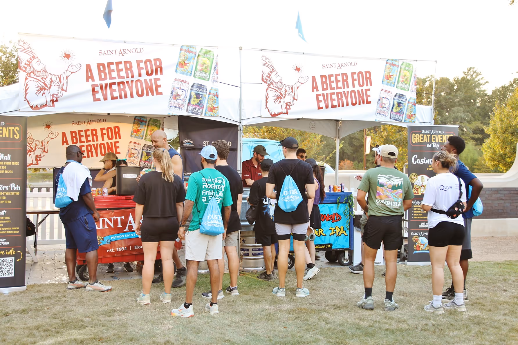 People standing in line at a Saint Arnold beer booth outdoors with banners reading 'A Beer for Everyone'.