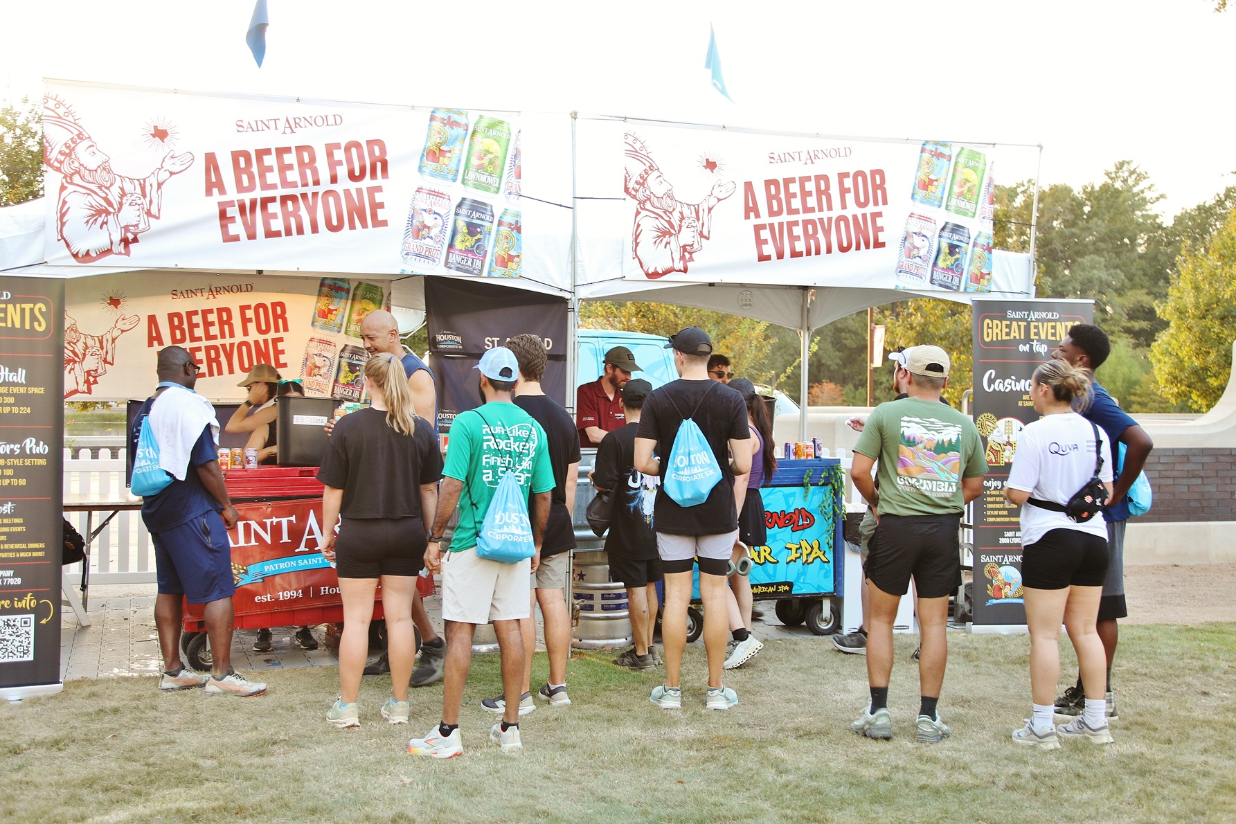 People standing in line at a Saint Arnold beer booth outdoors with banners reading 'A Beer for Everyone'.