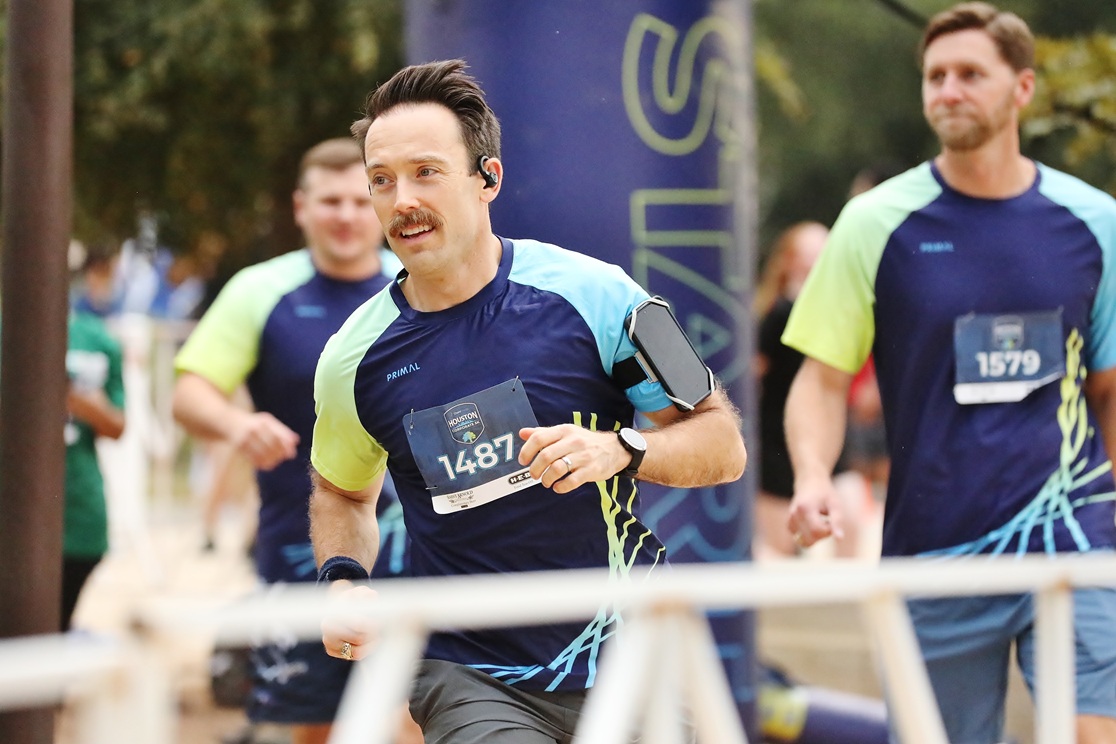 Male runners in blue and yellow athletic shirts participating in a race event near a start line.