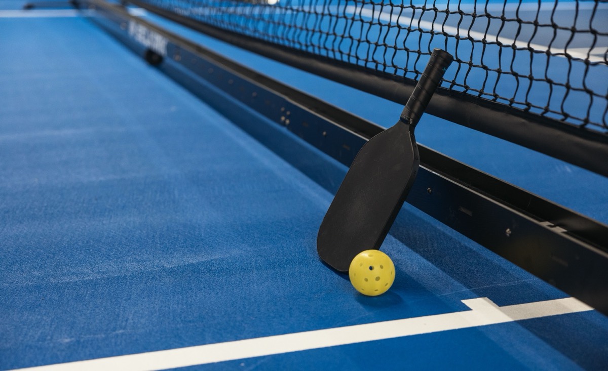 Pickleball paddle and ball beside the net on an indoor court