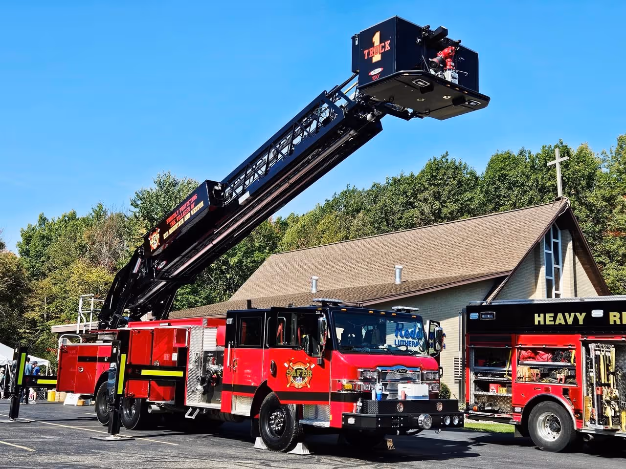 Red fire truck with an extended ladder platform parked in front of a building with a cross on its roof.