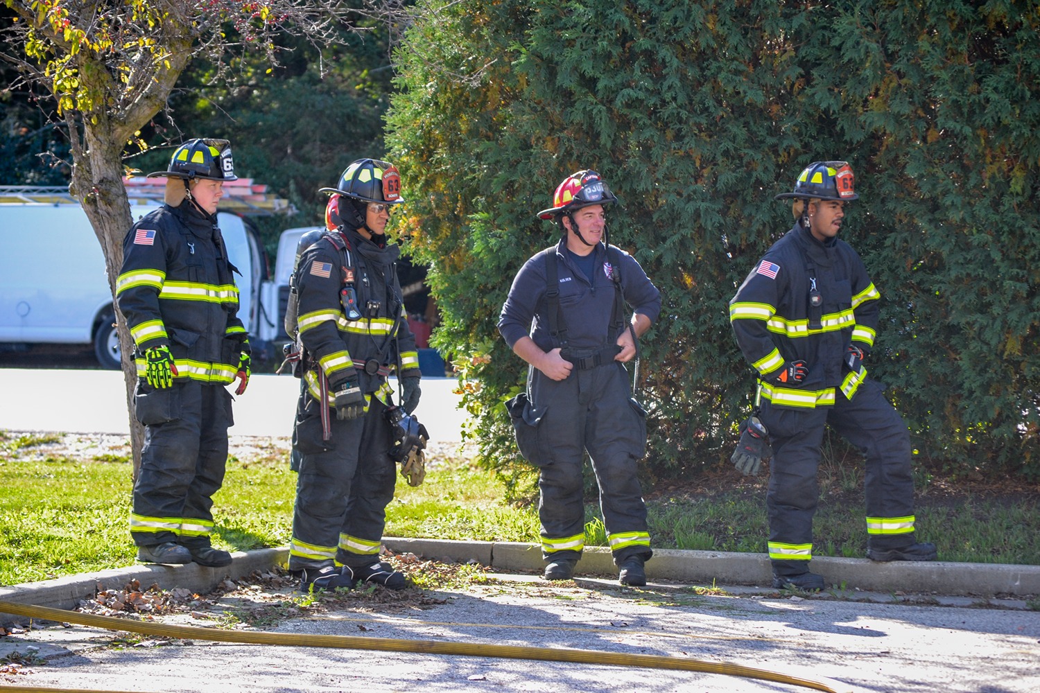 Firefighter on Engine 21 spraying water to extinguish large flames and smoke with tree branches overhead.