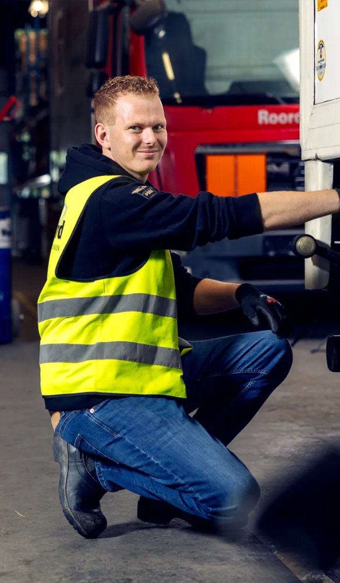 Cursist in geel veiligheidshesje zit gehurkt bij een vrachtwagen in de cursus hal van De Weerd Opleidingen
