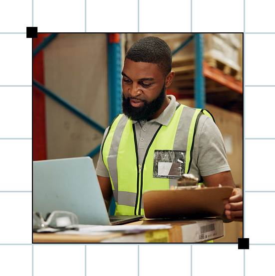 Warehouse worker with clipboard uses laptop
