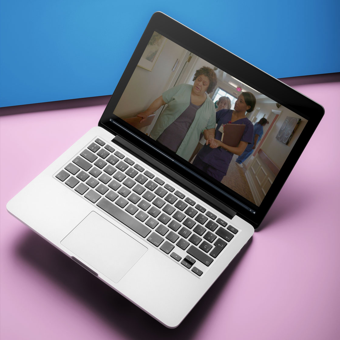 Laptop displaying a video of a nurse assisting an elderly woman walking down a hallway.