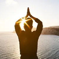 Человек стоит на фоне залива спиной к зрителю. Его руки сложены над головой в молитвенном жесте