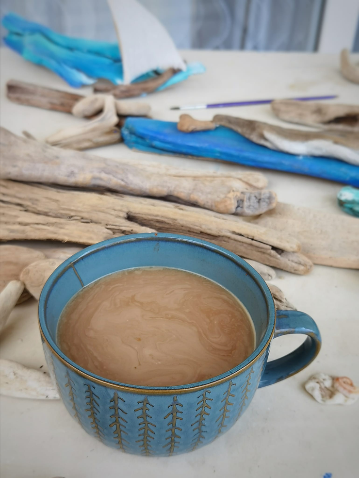 Голубая чашка с кофе стоит на белом столе. Рядом с ней коряга