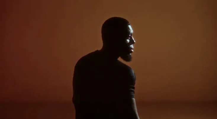 Silhouette of a man with a beard against a warm brown background.