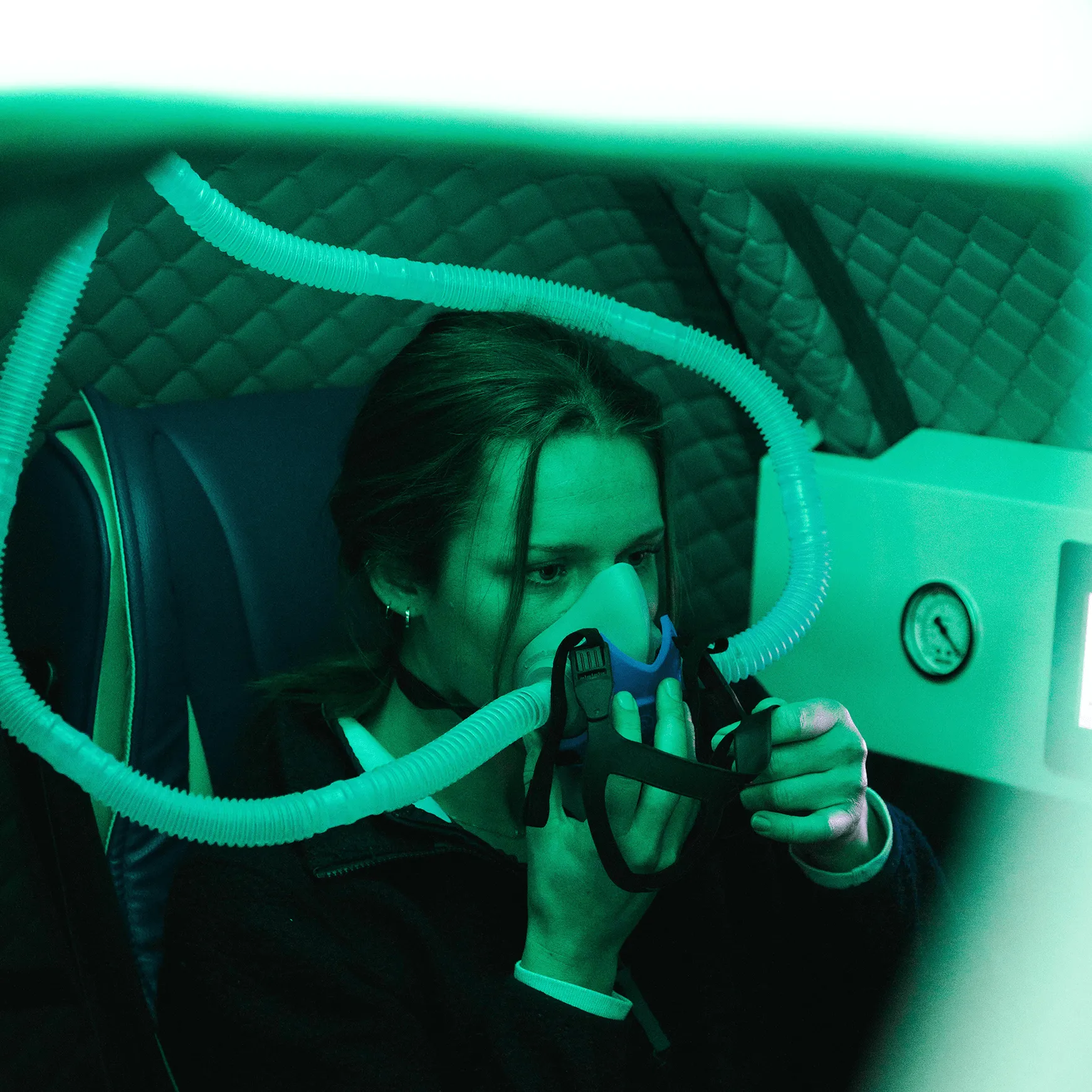 Woman wearing a breathing mask connected to a medical device in a padded enclosure.