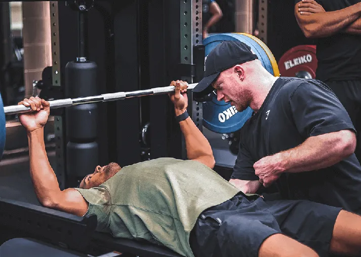 A person lying on a bench press lifting weights while a trainer spots them in a gym.