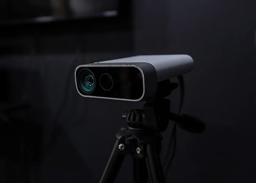 Digital camera or 3D scanner device mounted on a tripod with a dark background.