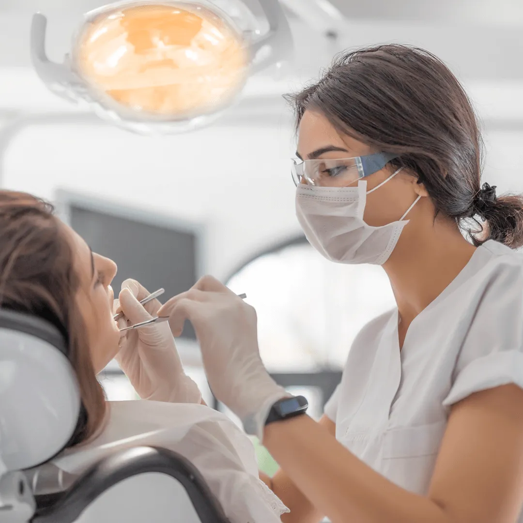 Dentist wearing mask and protective glasses examining a patient's teeth in a dental clinic.
