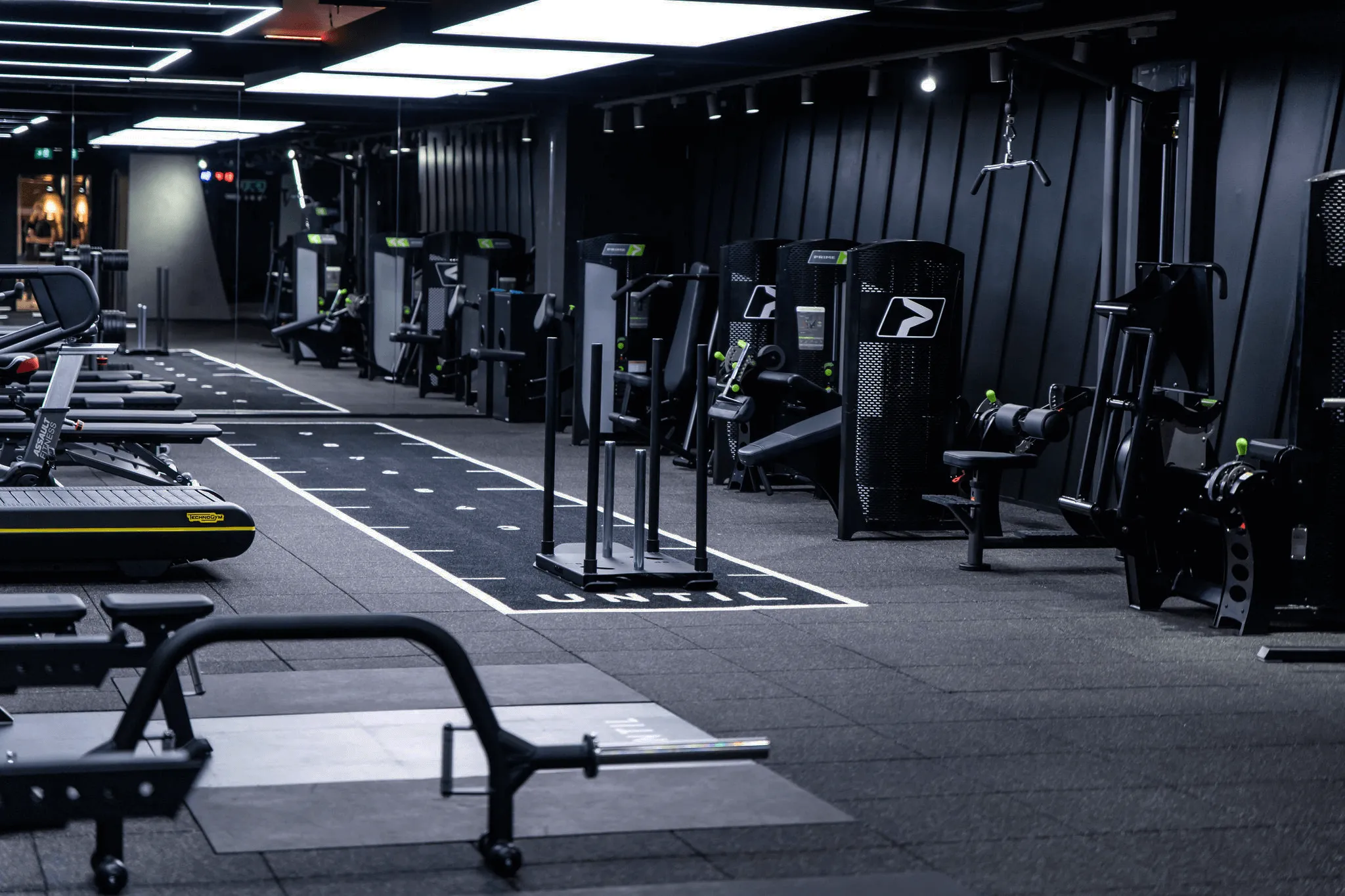 Modern gym interior with various weight machines, benches, treadmill, and workout area with sled push on rubber flooring.
