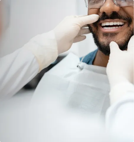Dentist wearing gloves examining a smiling patient's teeth during a dental checkup.