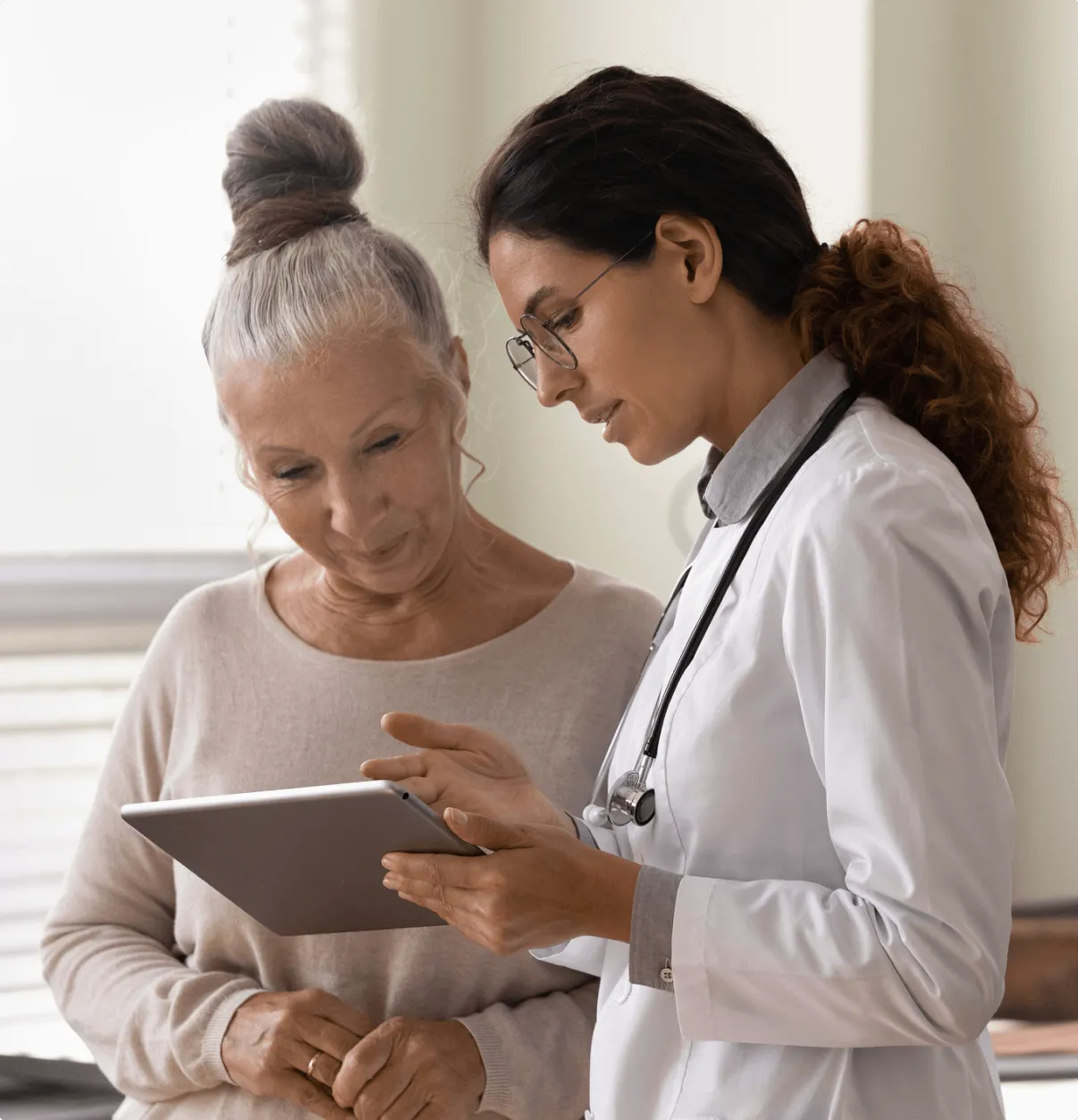 Female doctor showing information on a tablet to an elderly woman in a clinical setting.