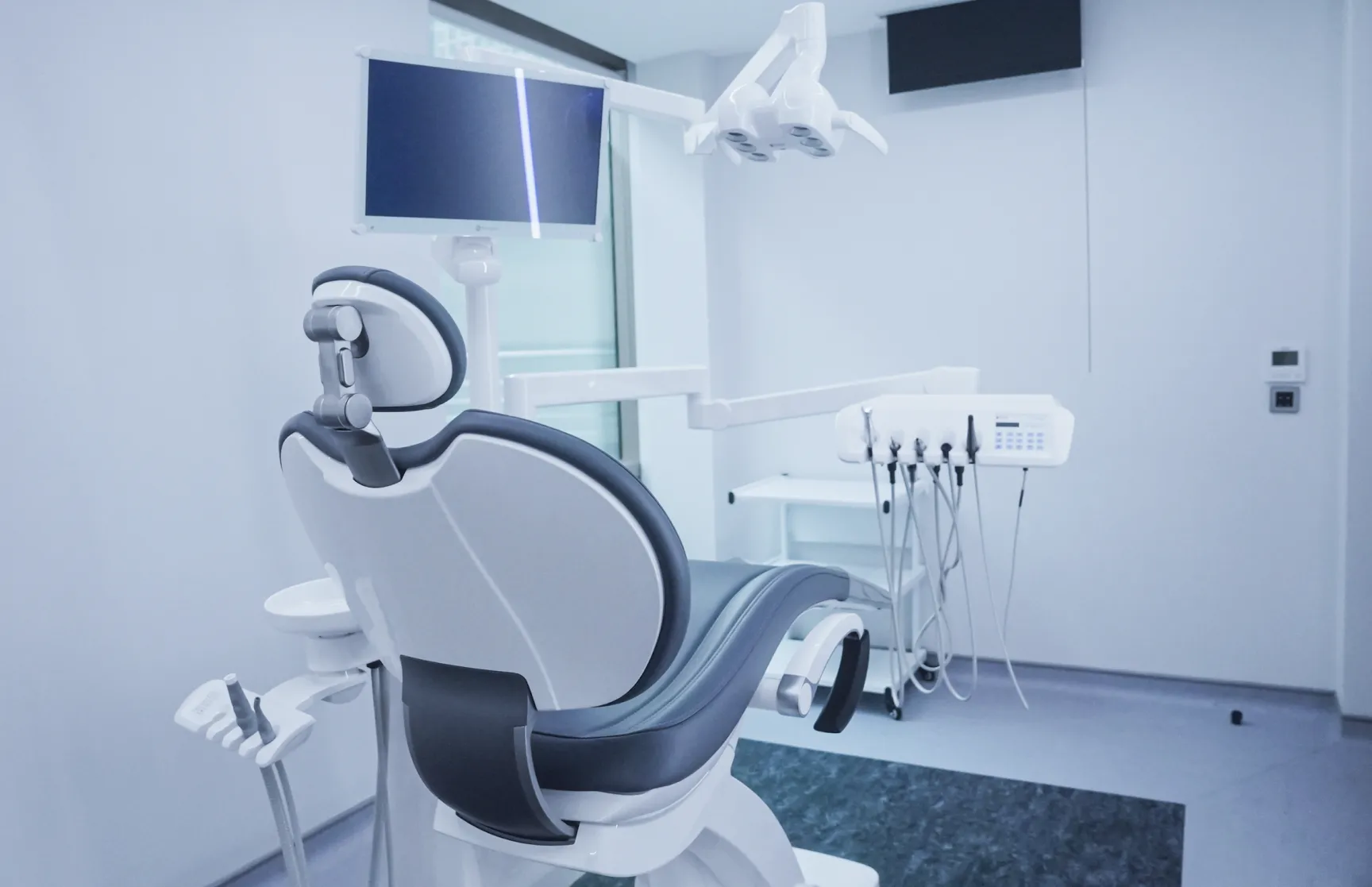 Modern dental clinic with an empty dental chair, overhead light, monitor, and dental instruments.