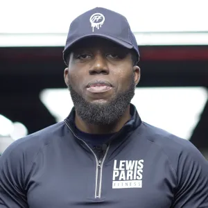 Man wearing a navy cap and navy zip-up jacket with 'Lewis Paris Fitness' logo.