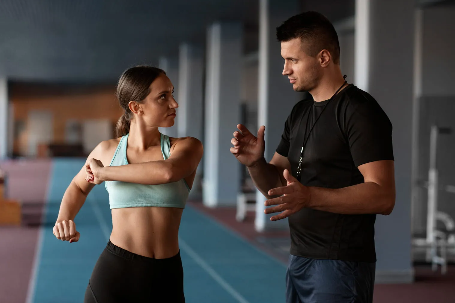 Female athlete stretching her arm while a male coach instructs her indoors on a running track.