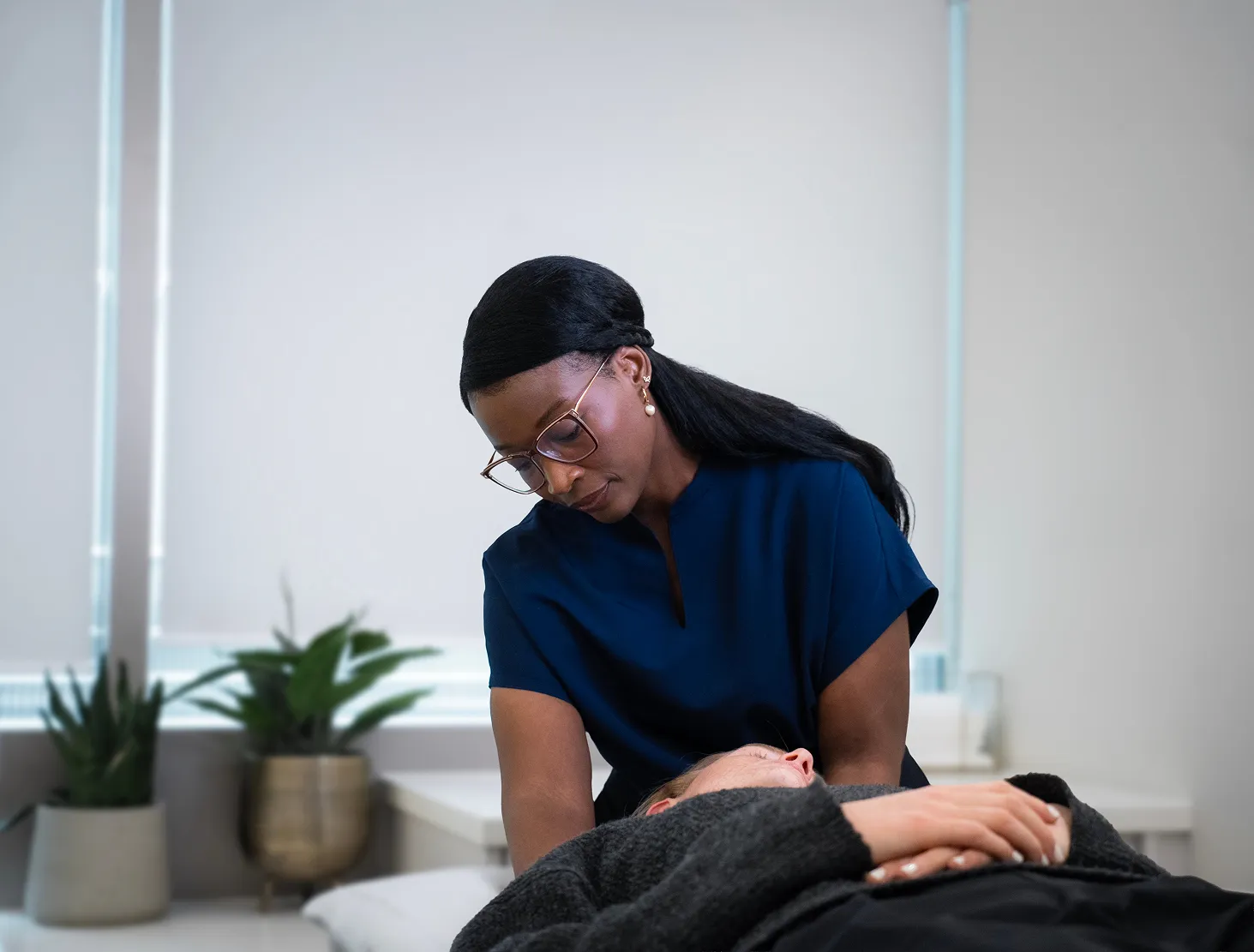 Therapist in blue scrubs attentively looking at a patient lying on a treatment table.