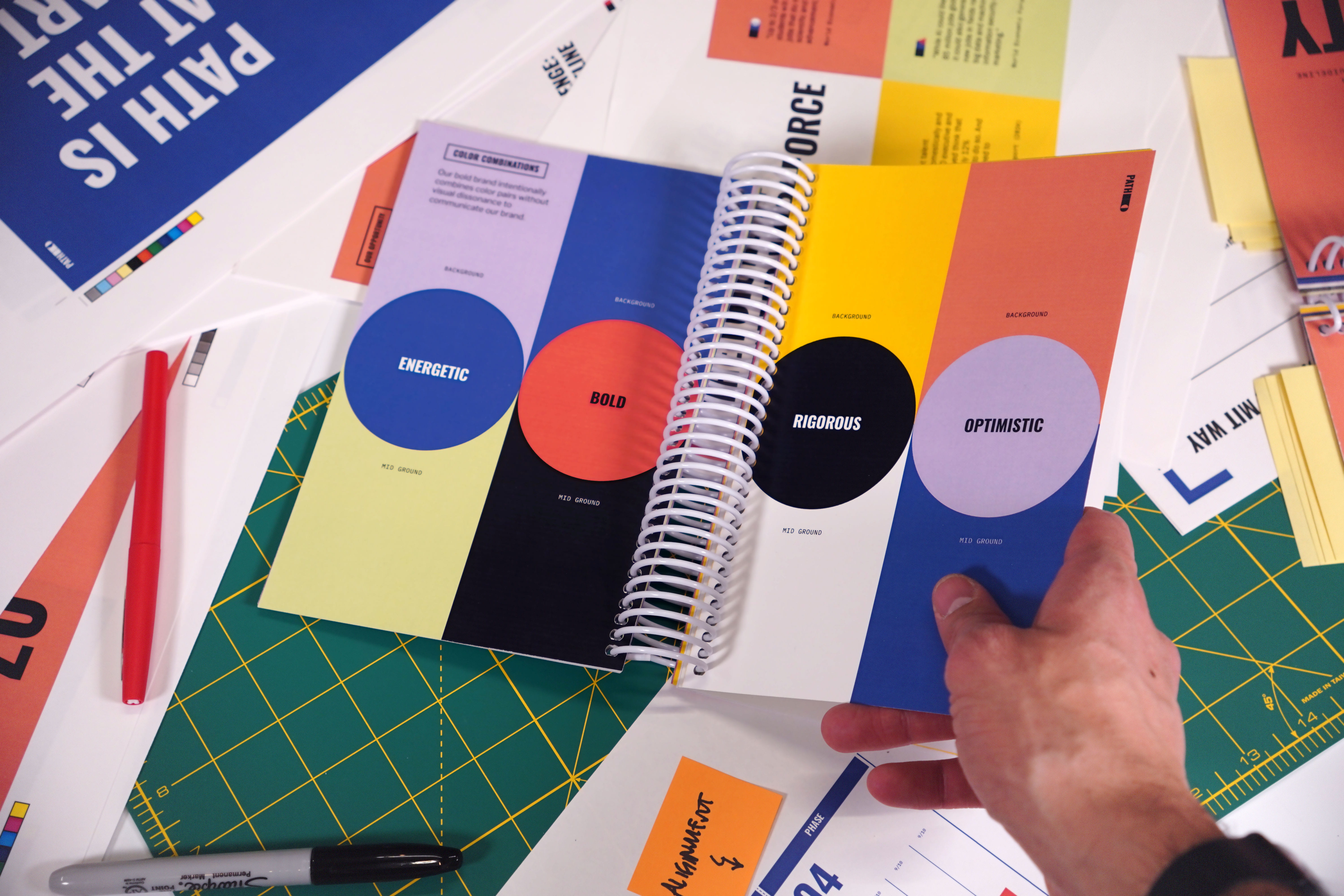 Hand holding book over messy work surface showing brand color usage