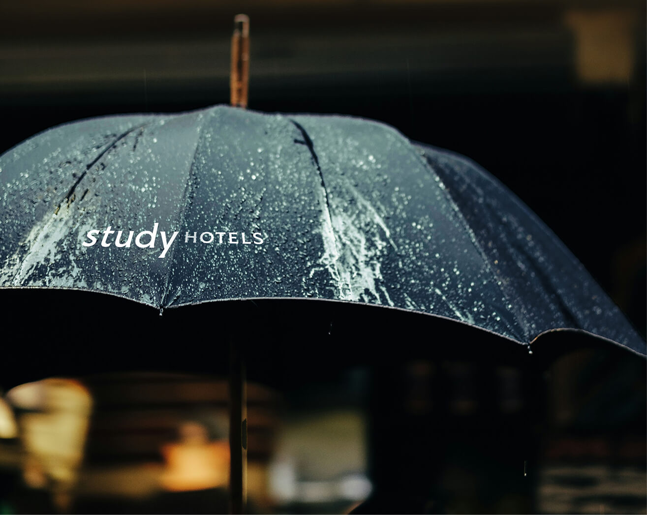 Dark sea green umbrella beading with rain showing Study Hotels branding