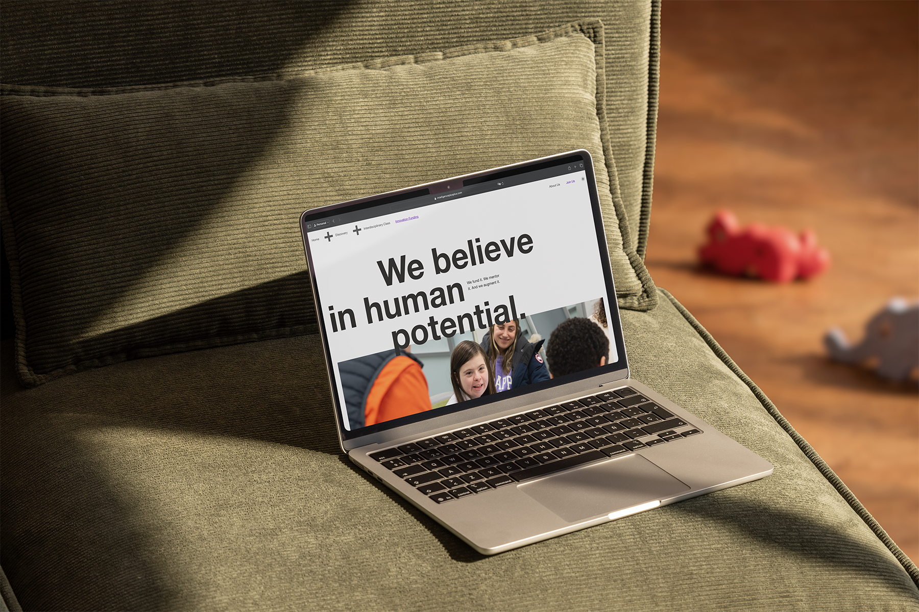A laptop open on a couch. The browser pages says "We believe in human potential"