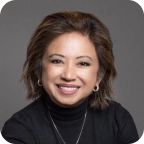 Smiling woman with short brown hair wearing black turtleneck and silver hoop earrings.